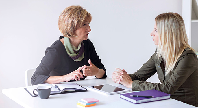 Two people in discussion, sat at a table with an iPad and a hot drink cup