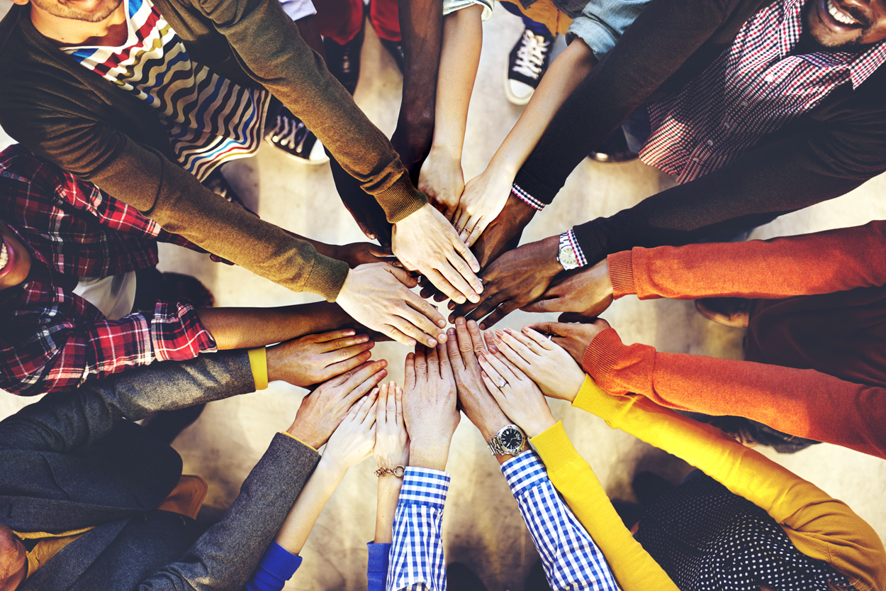 Looking down on a circle of people, as they all put their arms into the center