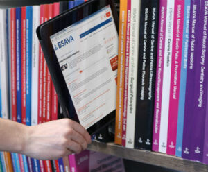 A digital tablet displaying the BSAVA online library website. It's been removed from between other BSAVA printed books, held on a shelf.