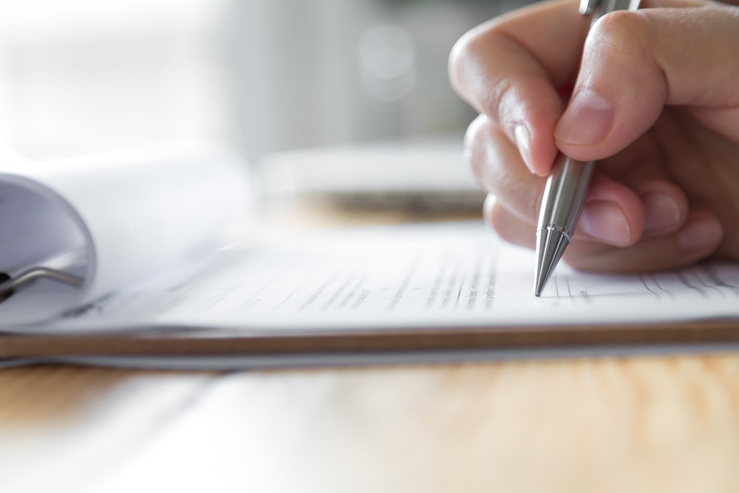 A person holding a metal pen, filling out a form