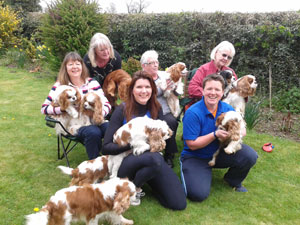 Six people smiling, all holding dogs outside in a garden