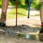 Closeup of hiking boots and walking poles of a pair of people as they walk through the countryside